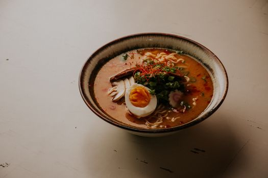 Appetizing ramen noodle soup with a soft-boiled egg, herbs, and spices in a ceramic bowl.