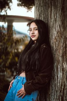 Teen model with long hair poses in nature, wearing a jacket and jeans, embodying calm and casual fashion.
