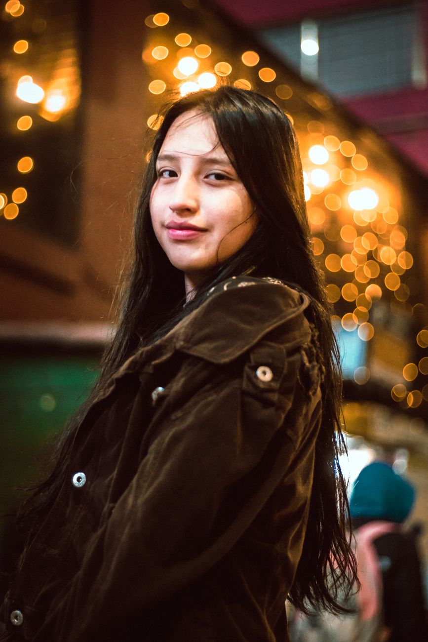 Portrait of a young woman in a nighttime street scene with bokeh lights.