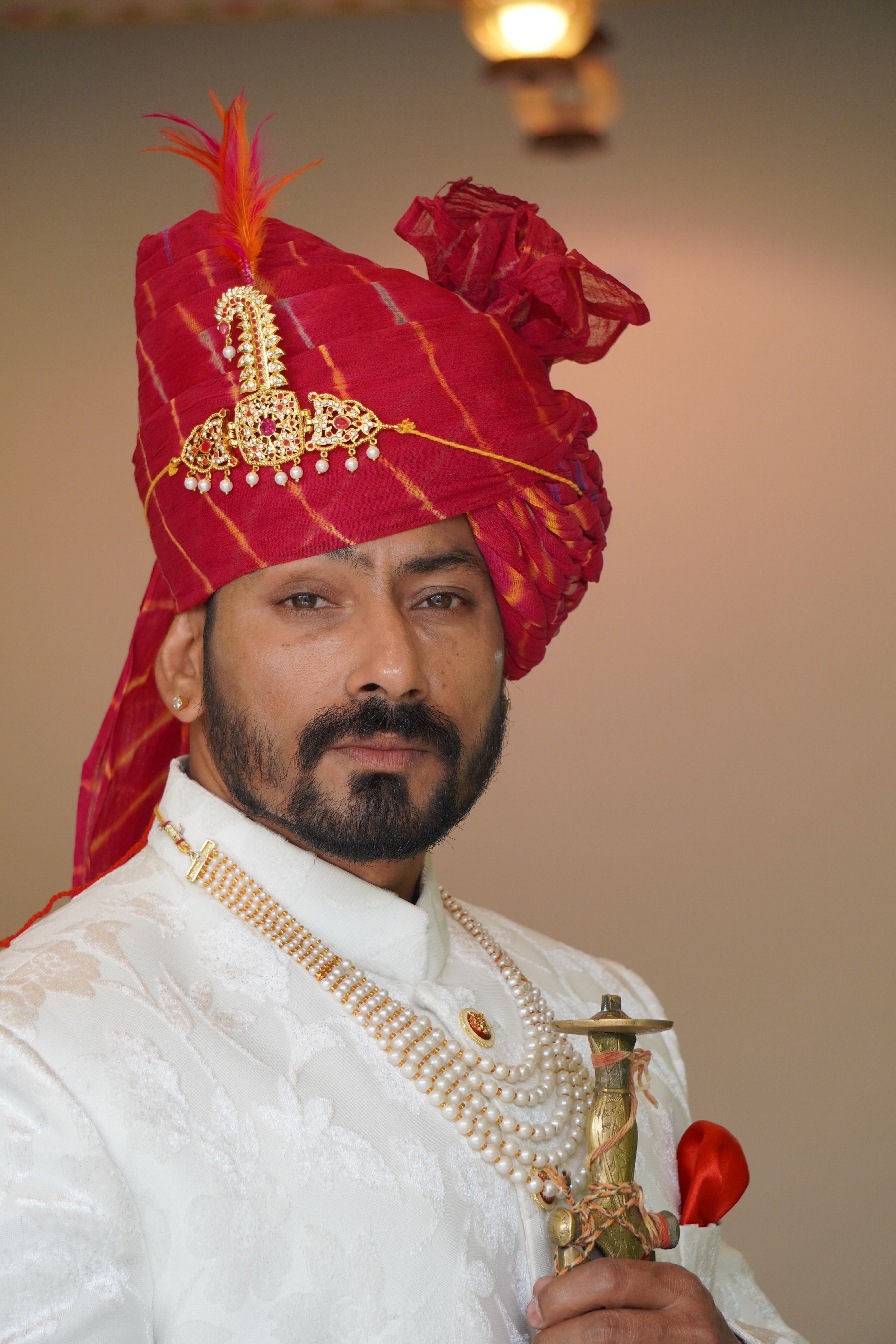 Close-up portrait of a handsome groom in traditional attire wearing a red turban.