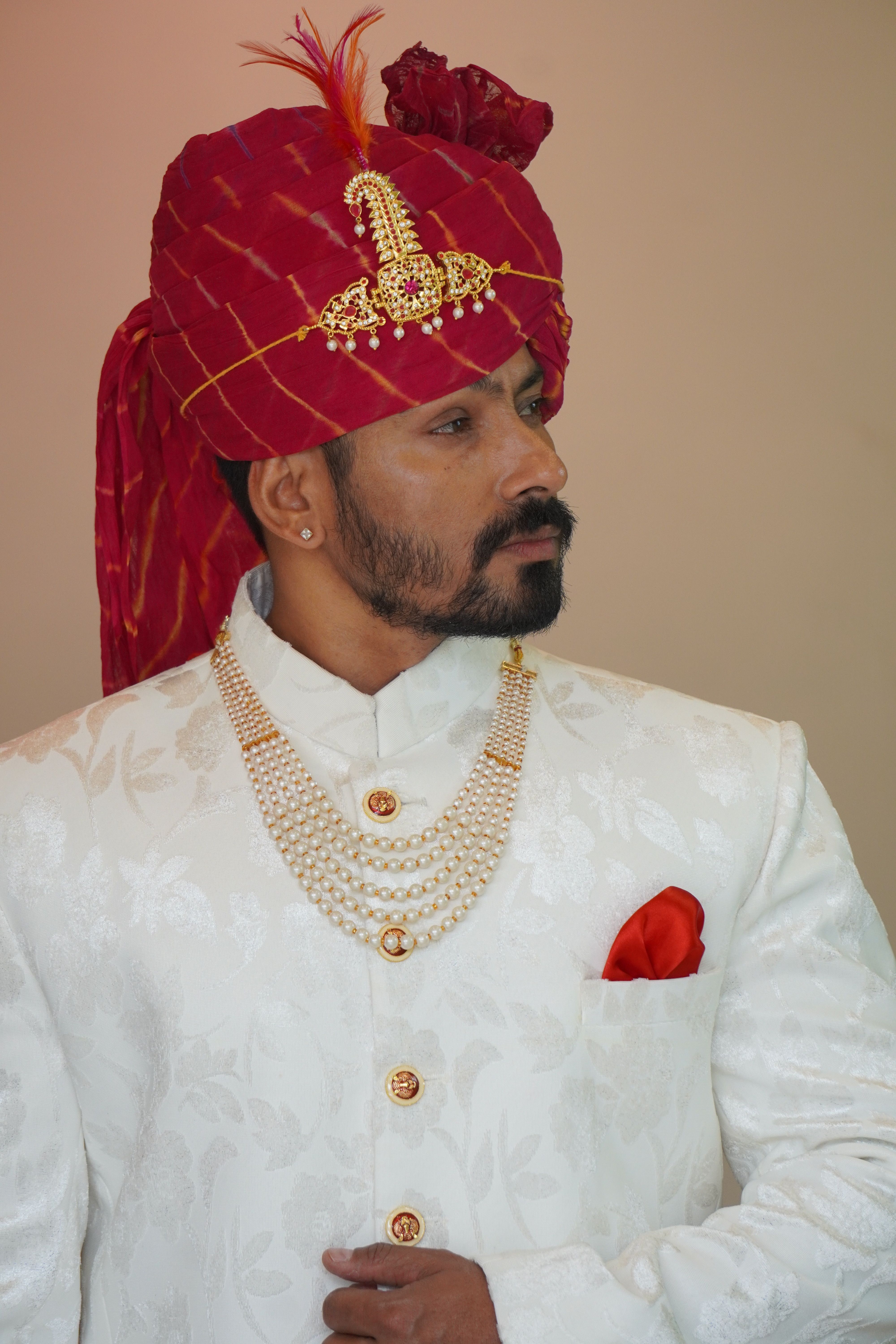 Man wearing an ornate red turban and white gown, exuding sophistication and luxury.