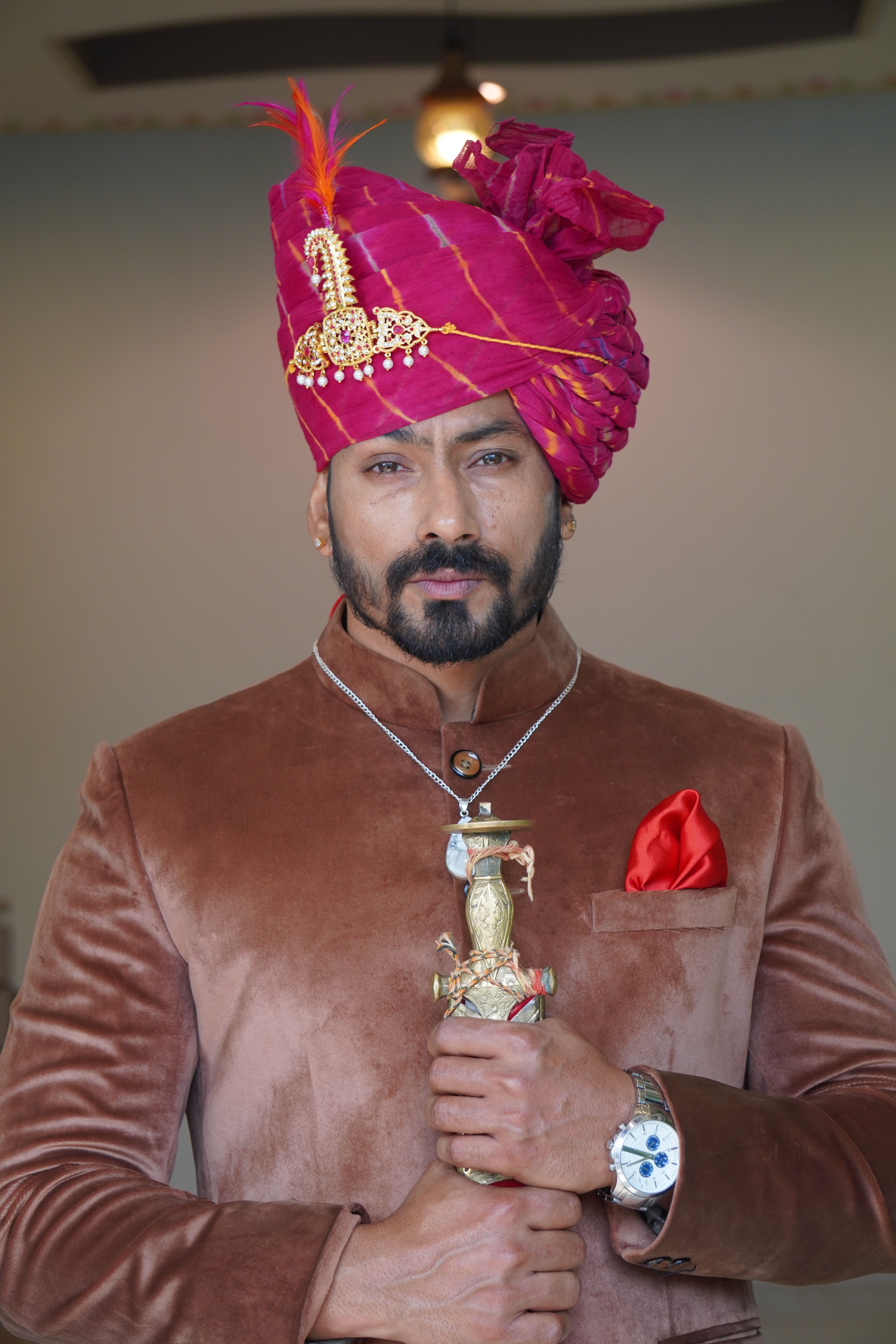 A man in velvet attire with a pink turban and accessories, exuding elegance and sophistication.