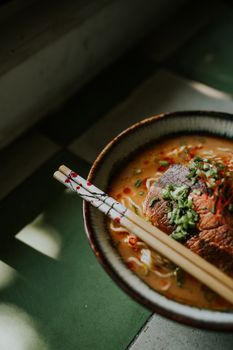 A gourmet Japanese ramen bowl with beef, noodle soup, and chopsticks in a cozy setting.