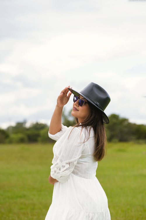 Woman Wearing a Black Hat and a White Dress Posing on a Green Filed