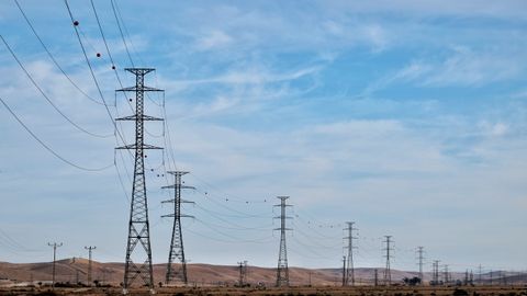Transmission towers in a desert landscape with blue skies, showcasing energy infrastructure.