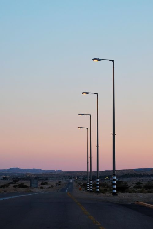 Free A peaceful view of streetlights lining a deserted road at sunset in a desert landscape. Stock Photo