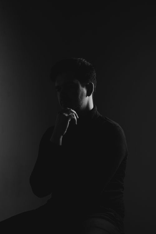 Free Black and white silhouette of a man in deep thought with hand on chin, studio lighting. Stock Photo