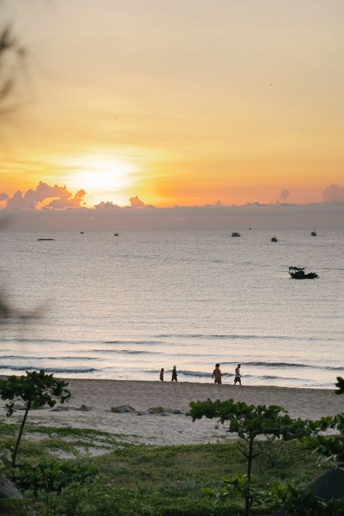 Free A peaceful beach scene at sunset with silhouettes of people walking along the shore. Stock Photo