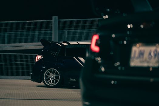 Dramatic image of sports cars parked at night, featuring sleek designs and vivid rear lights.