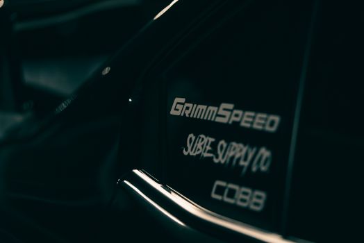 A dark, modern sports car featuring GrimmSpeed and Subie Supply Co branding.