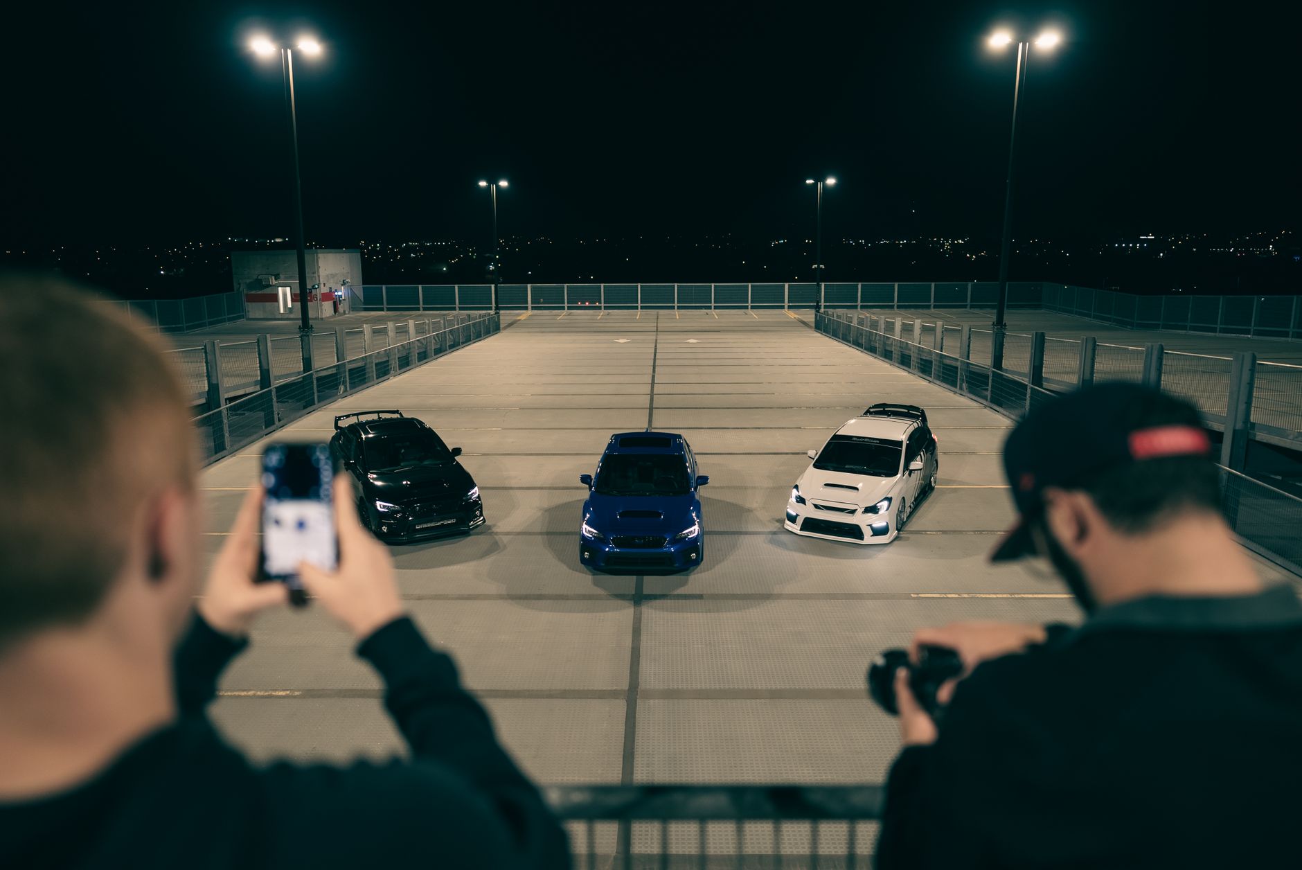 Nighttime shot of three sports cars in a parking structure, with photographers capturing the moment.