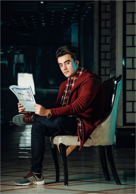 Young man in fashionable attire posing indoors holding a newspaper, exuding modern style. Young man in fashionable attire posing indoors holding a newspaper, exuding modern style.
