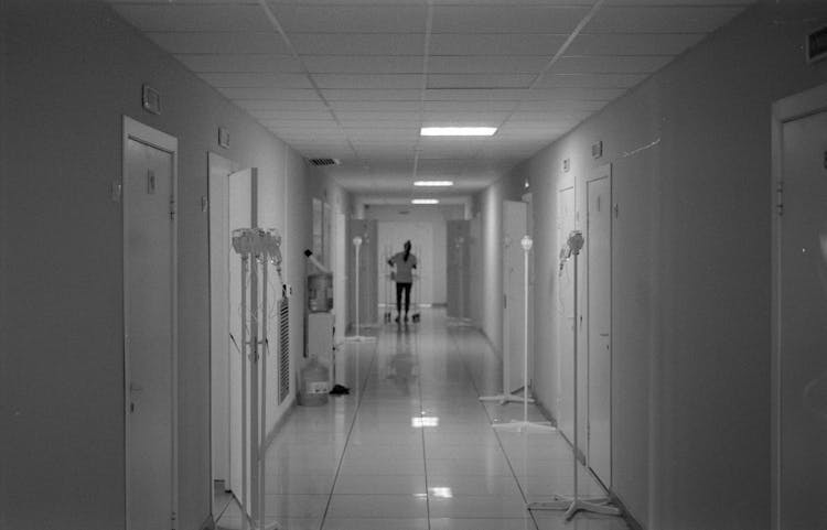 Black And White Photo Of Nurse Standing At End Of Hospital Hallway