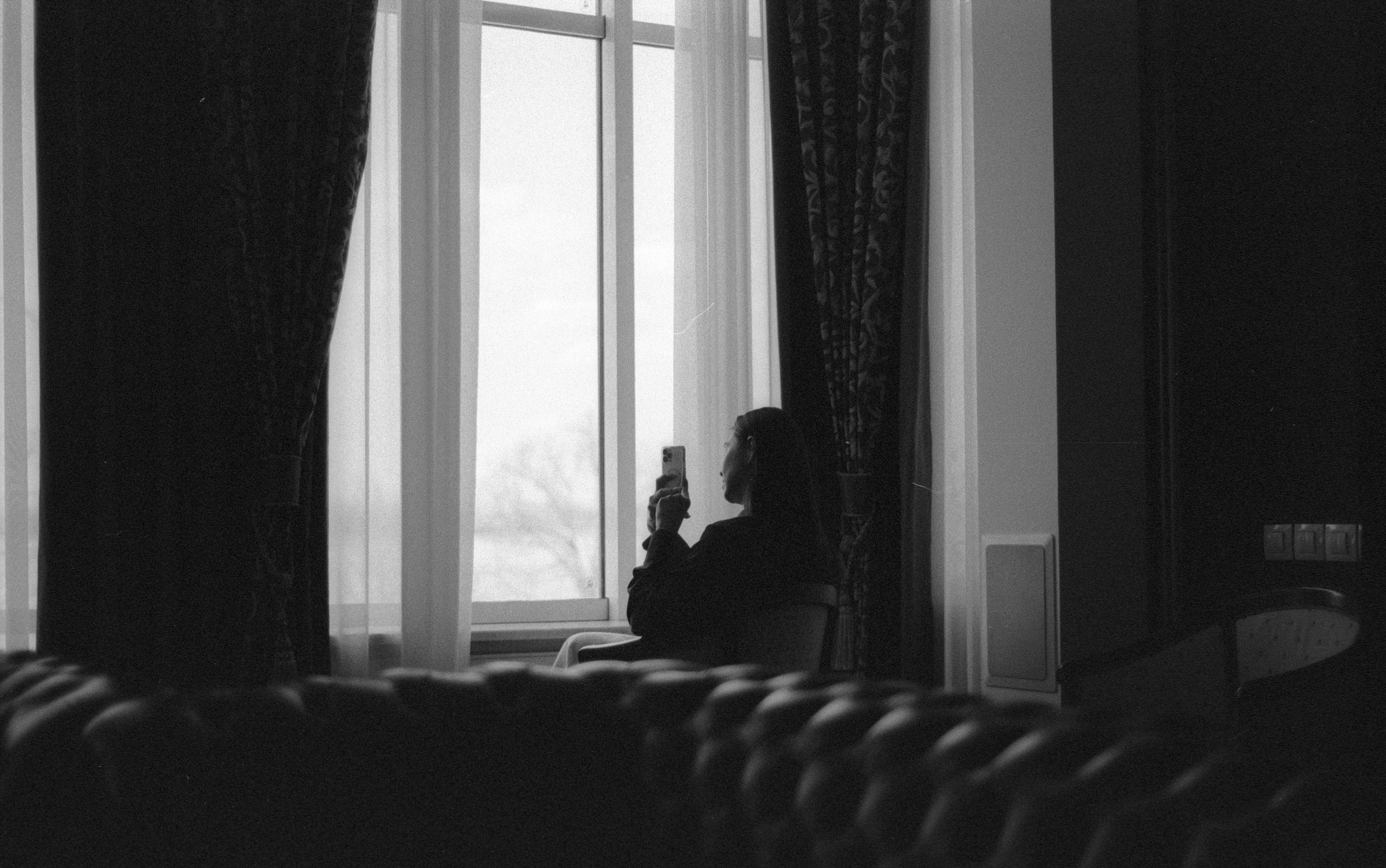 A Woman Sitting by the Window and Holding a Smartphone · Free Stock Photo