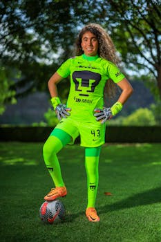 Woman goalkeeper in green sportswear standing on grass with soccer ball.