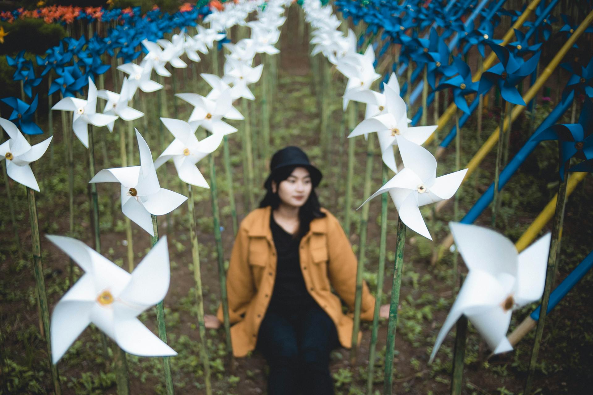 A woman sitting among rows of colorful pinwheels in a vibrant outdoor art installation.