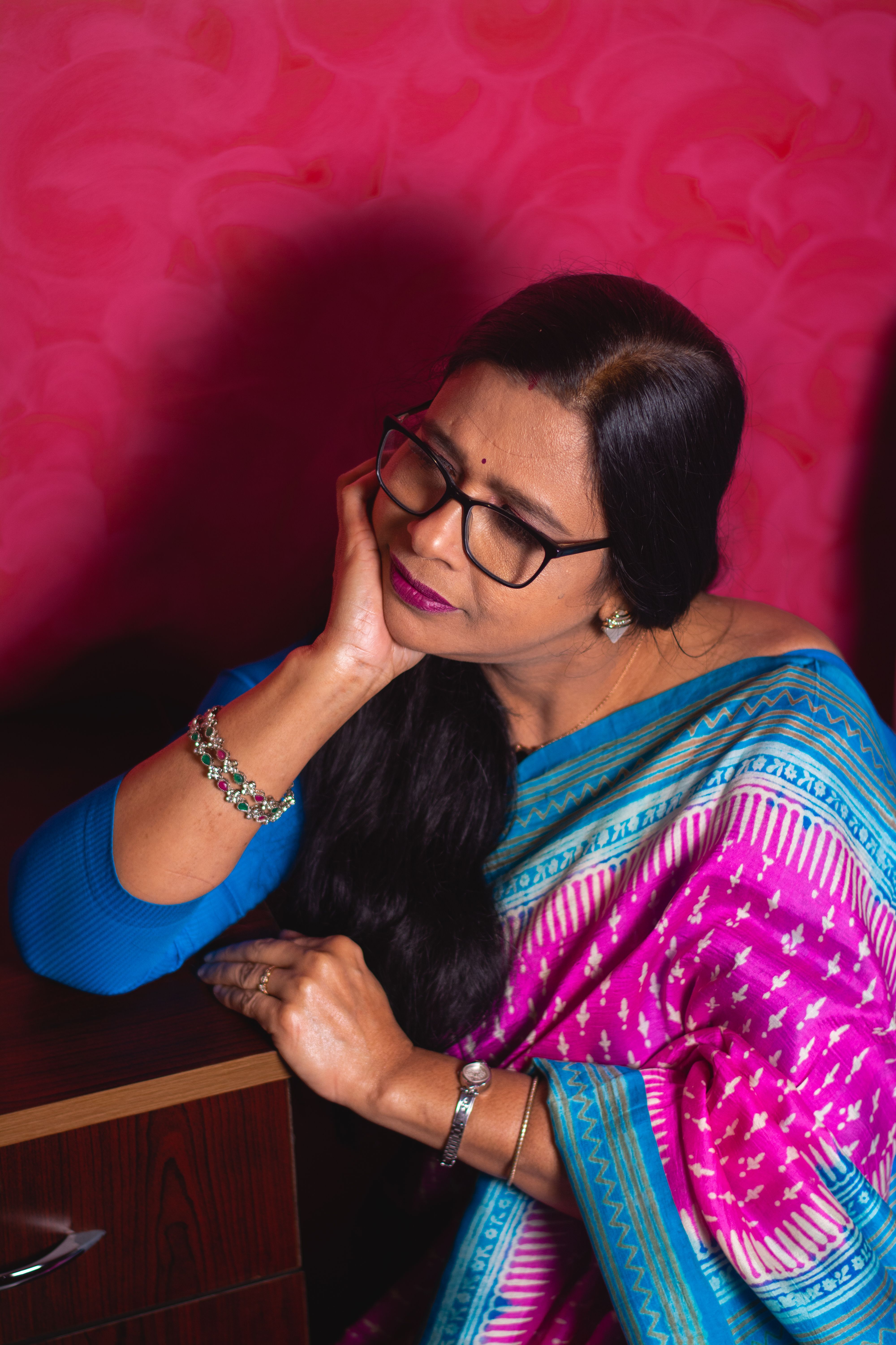 Portrait of a woman in traditional Indian attire, sitting thoughtfully indoors.