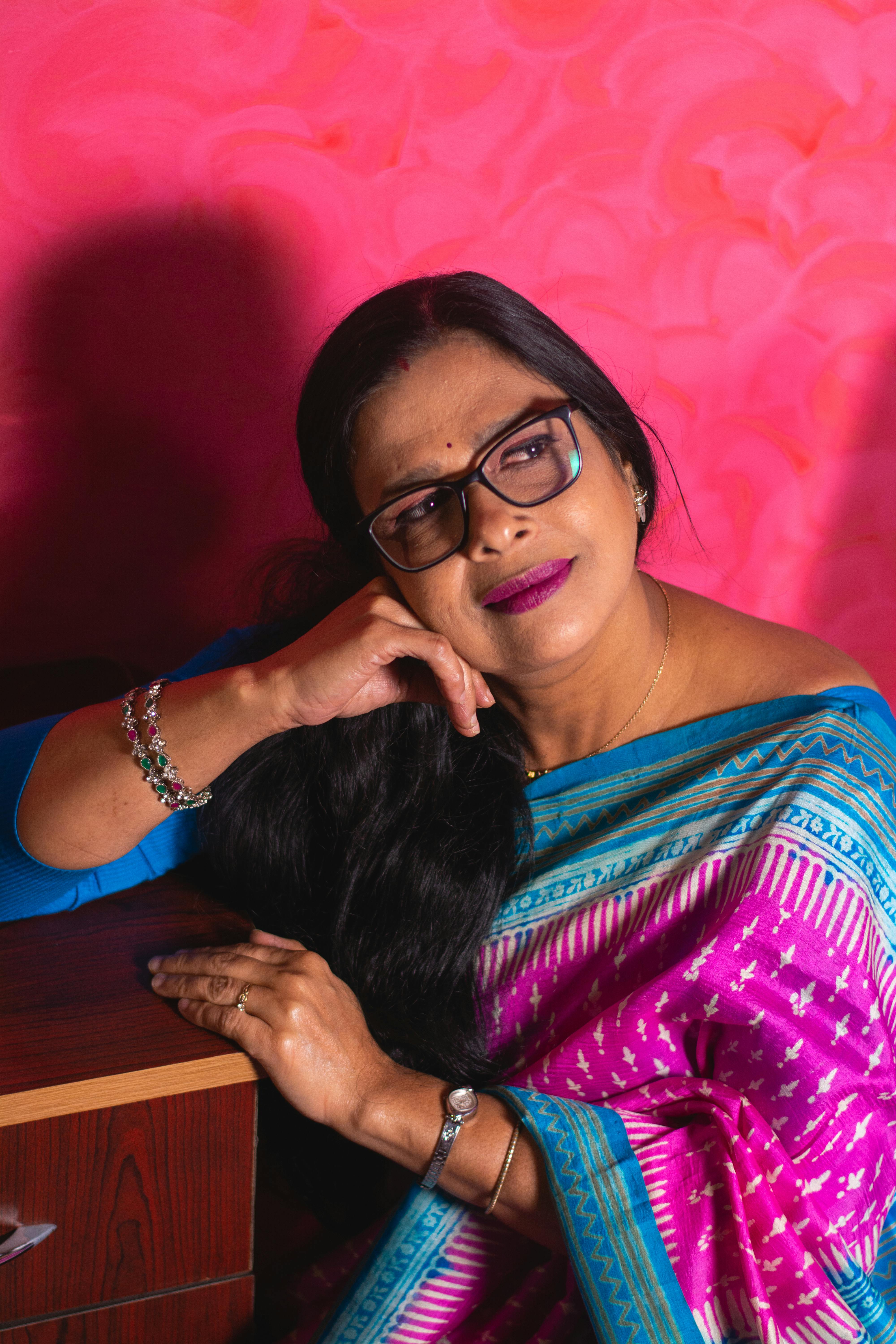 Portrait of an Indian woman in a vibrant saree, seated and smiling indoors.