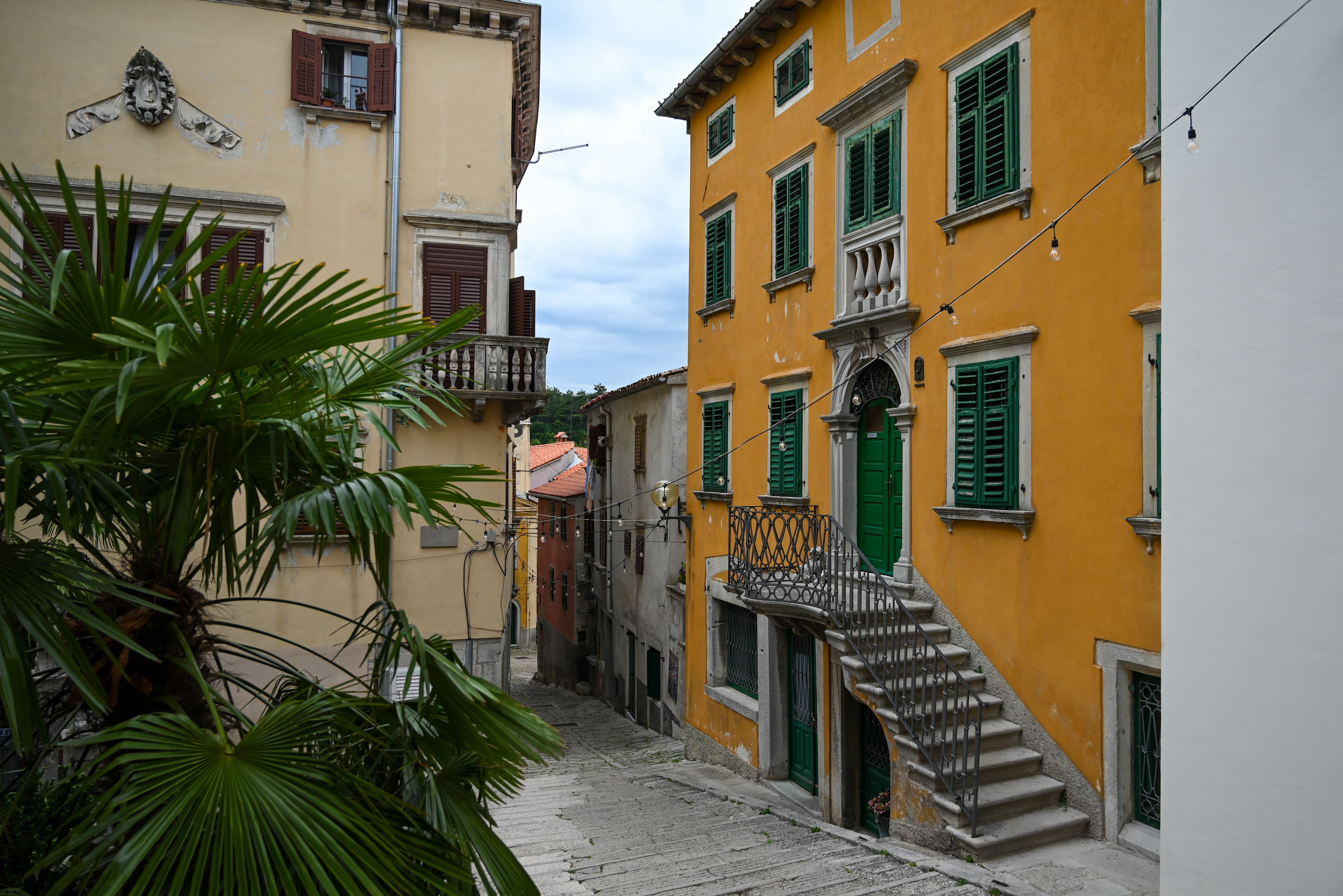 Explore the narrow, colorful streets of Labin with vibrant buildings and lush greenery.