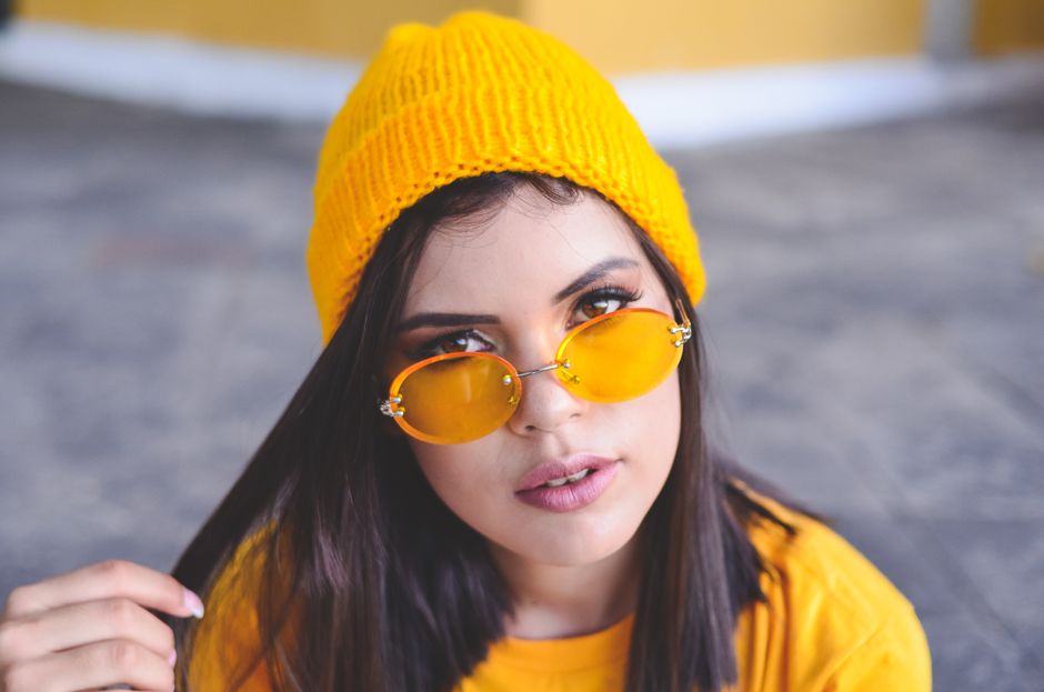 Fashionable woman wearing yellow sunglasses and hat poses confidently outdoors.