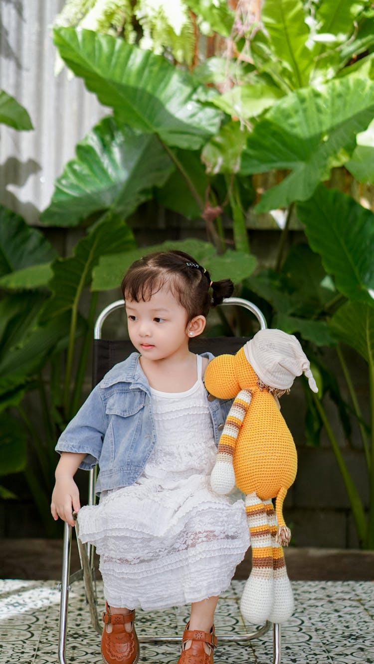 A Little Girl Holding A Teddy Bear And Sitting Outside 