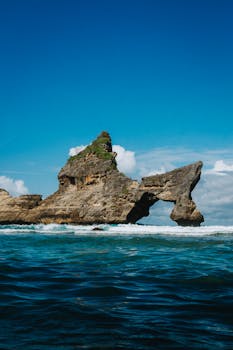 Striking natural arch formation over blue ocean waters at Atuh Beach in Nusa Penida, Bali.