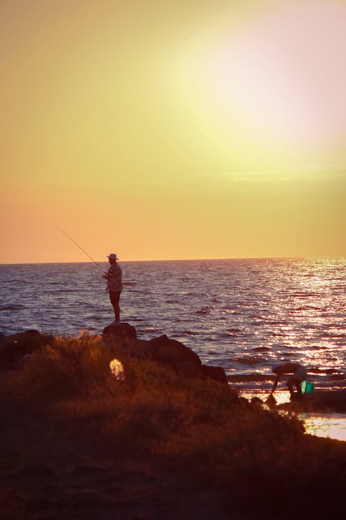 Man Standing on Rock Fishing on Sunset