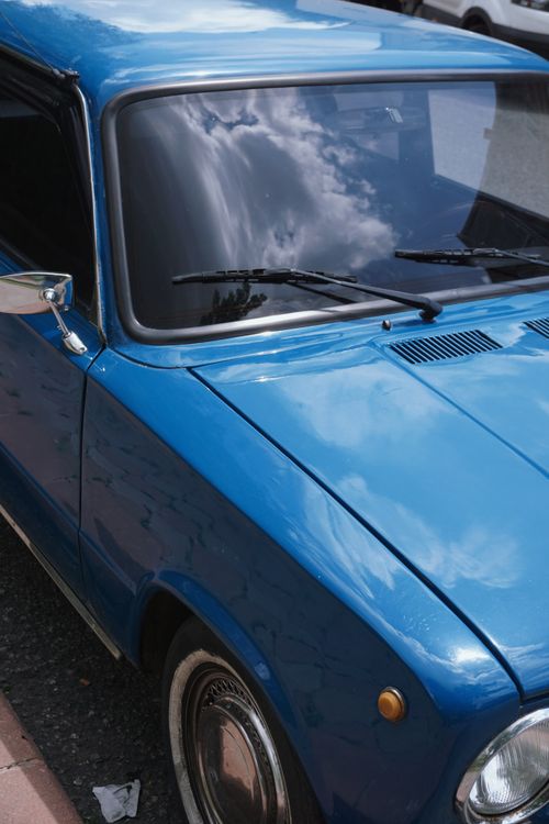 Free Close-up view of a classic blue car parked on a city street with cloudy reflections. Stock Photo
