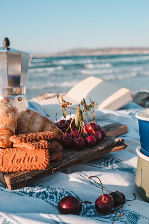 Free Fresh cherries, cookies, and croissants on a beach picnic setup, capturing a sunny day by the sea. Stock Photo