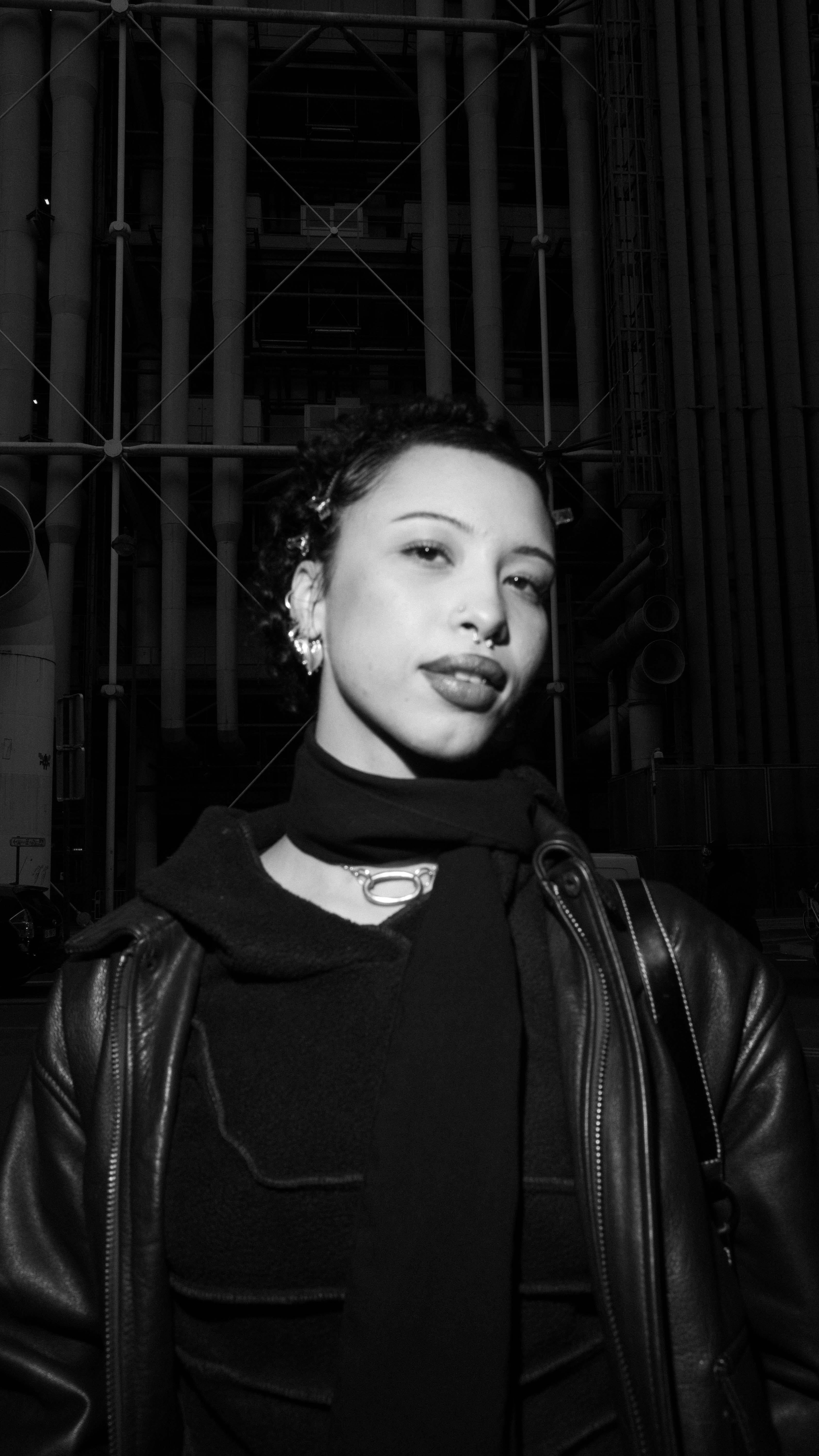 Black and white portrait of a stylish woman in urban setting, showcasing contemporary fashion.