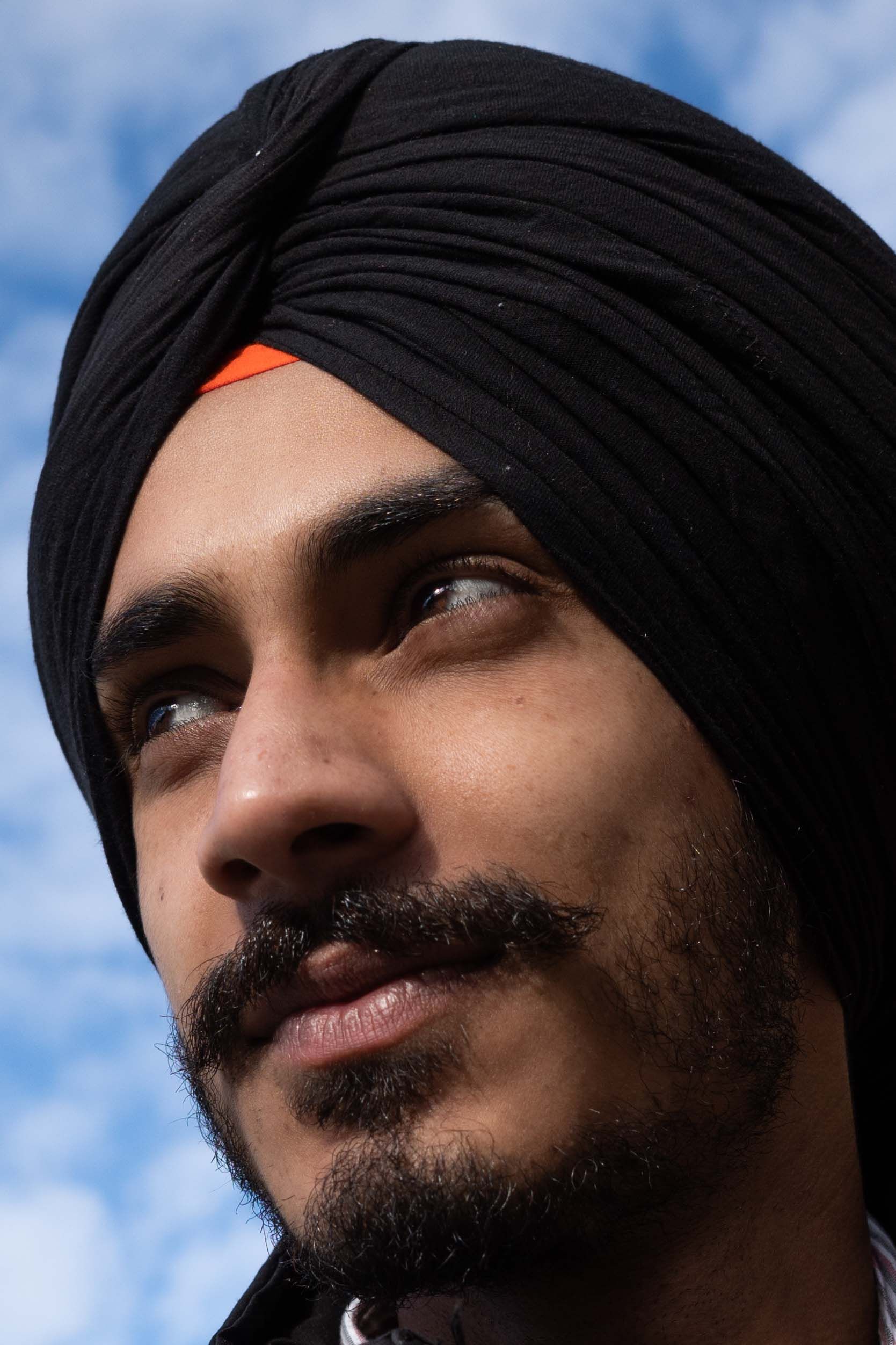 Close-up of a smiling man wearing a turban, looking into the distance against a bright blue sky.