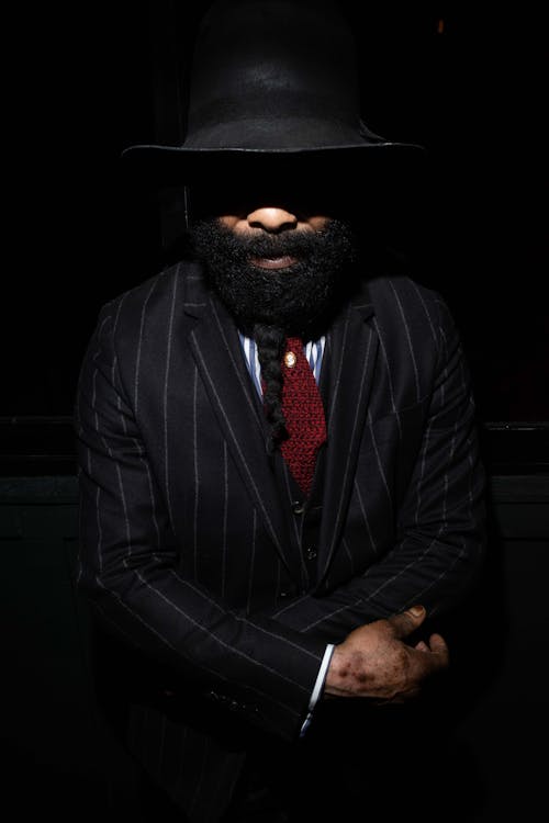 A Bearded Man in a Suit and a Hat Covering His Face