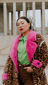 Fashionable woman in leopard print coat with pink fur collar poses confidently outdoors.