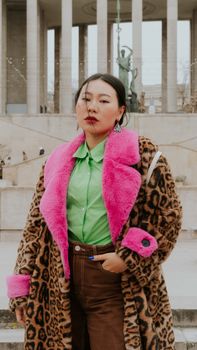 Fashionable woman in a vibrant pink-trimmed coat posing in an urban setting.
