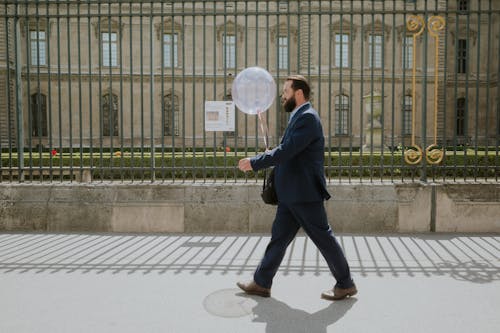 Man in Suit Walking with Balloon