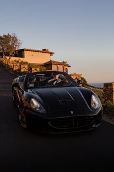 A black Ferrari California drives along a coastal road during golden hour, depicting luxury and adventure.