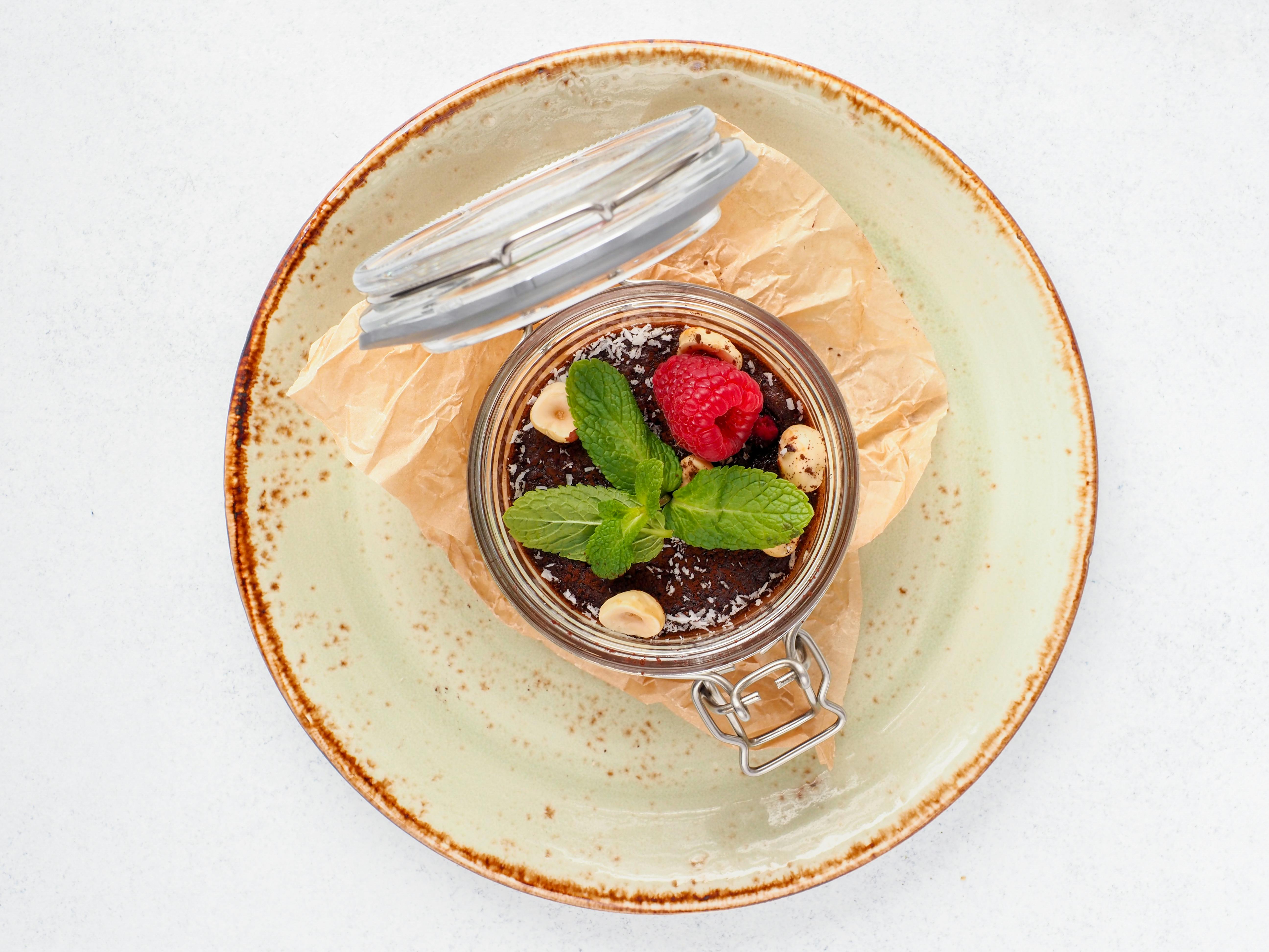 Indulge in a delectable gourmet chocolate dessert topped with fresh mint and raspberry in a stylish glass jar.