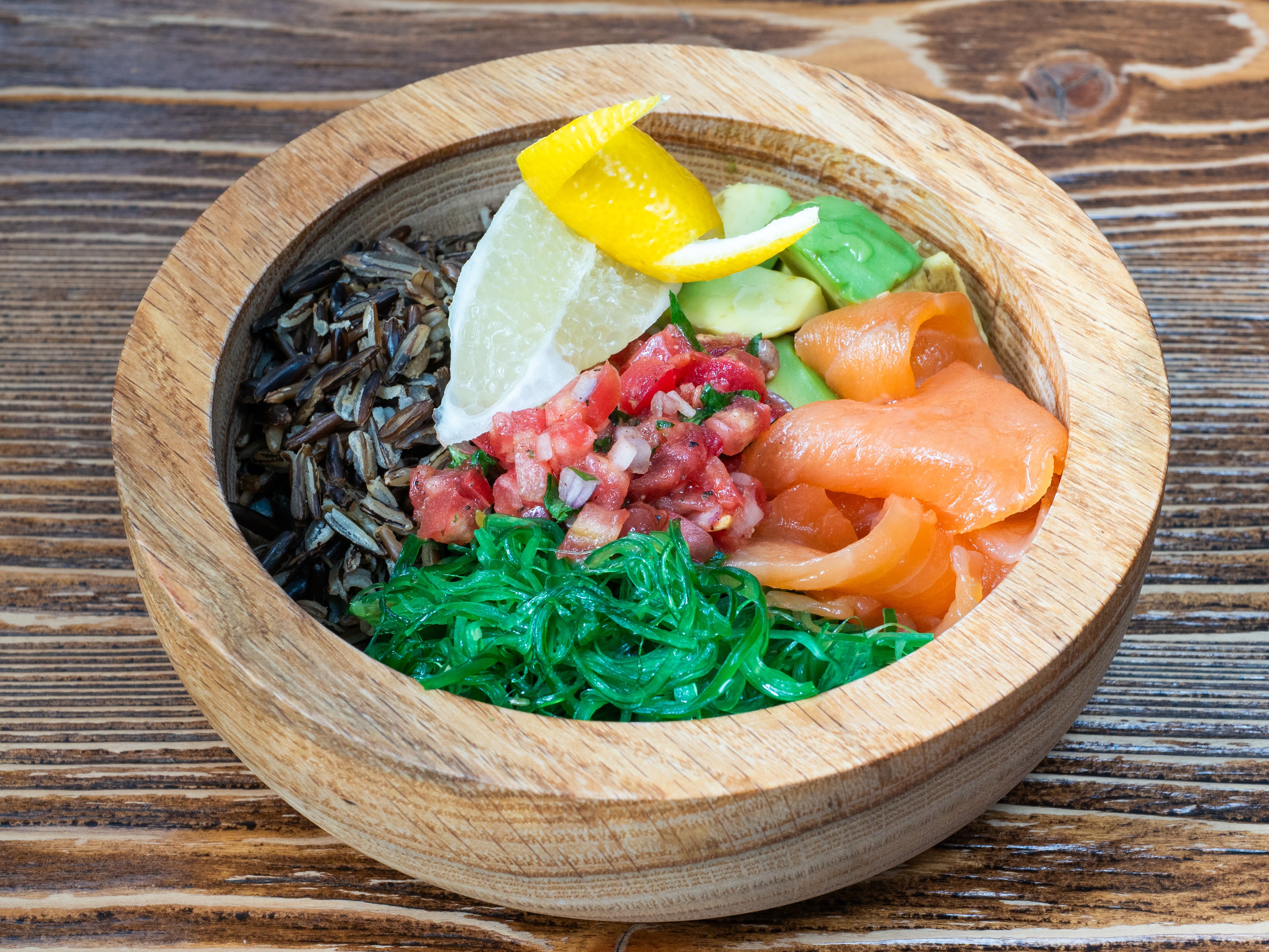 Vibrant poke bowl featuring salmon, avocado, and lemon slices in a wooden bowl.