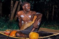 A young African man sitting outdoors with traditional tribal body paint and accessories at night in Uganda.