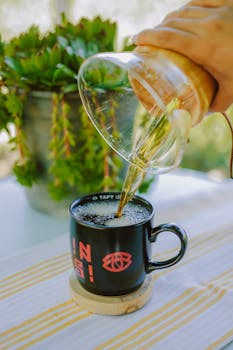 Close-up of fresh coffee being poured into a mug outdoors on a sunny day.