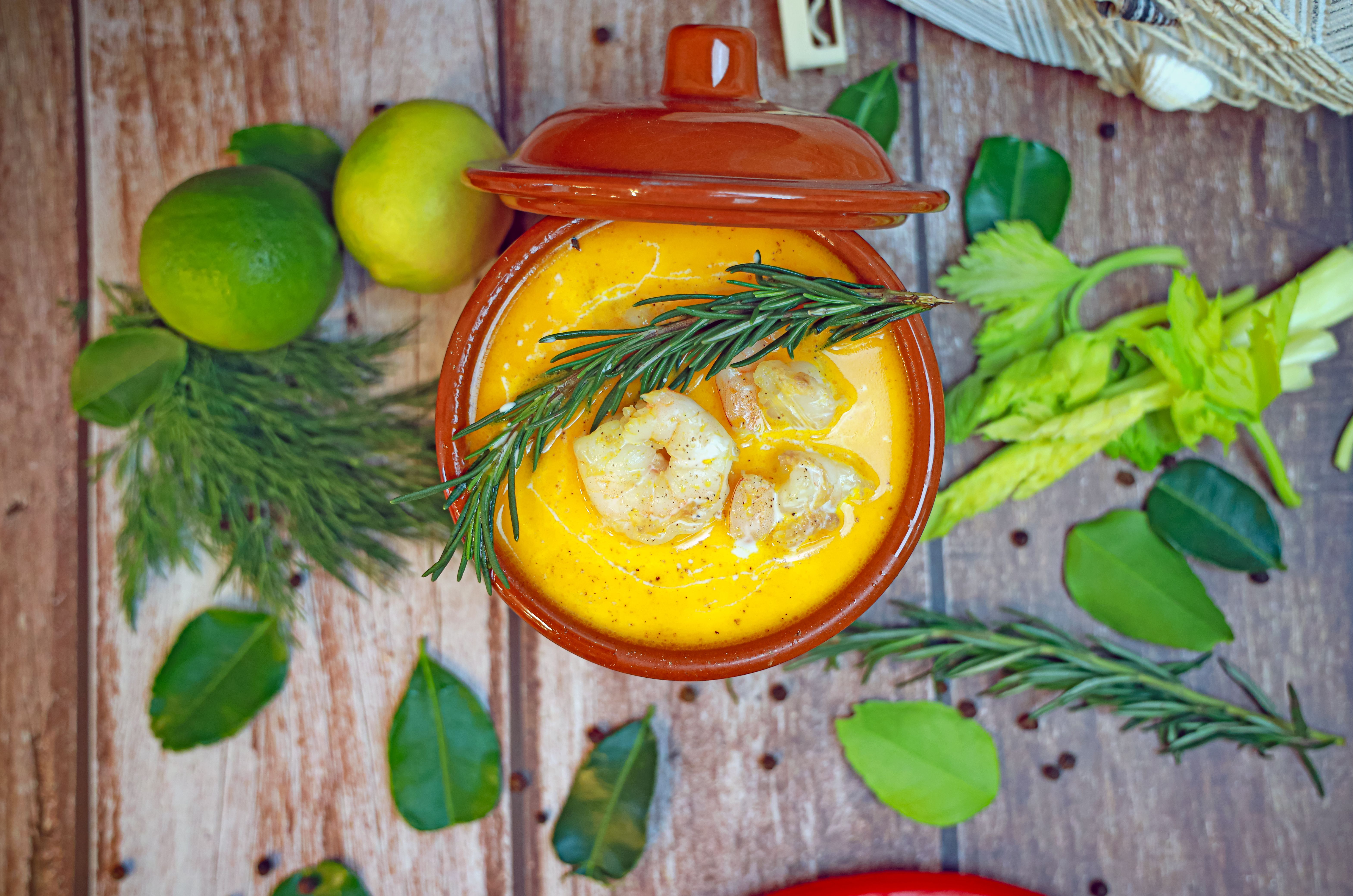 Top view of gourmet shrimp soup with rosemary and leafy greens.