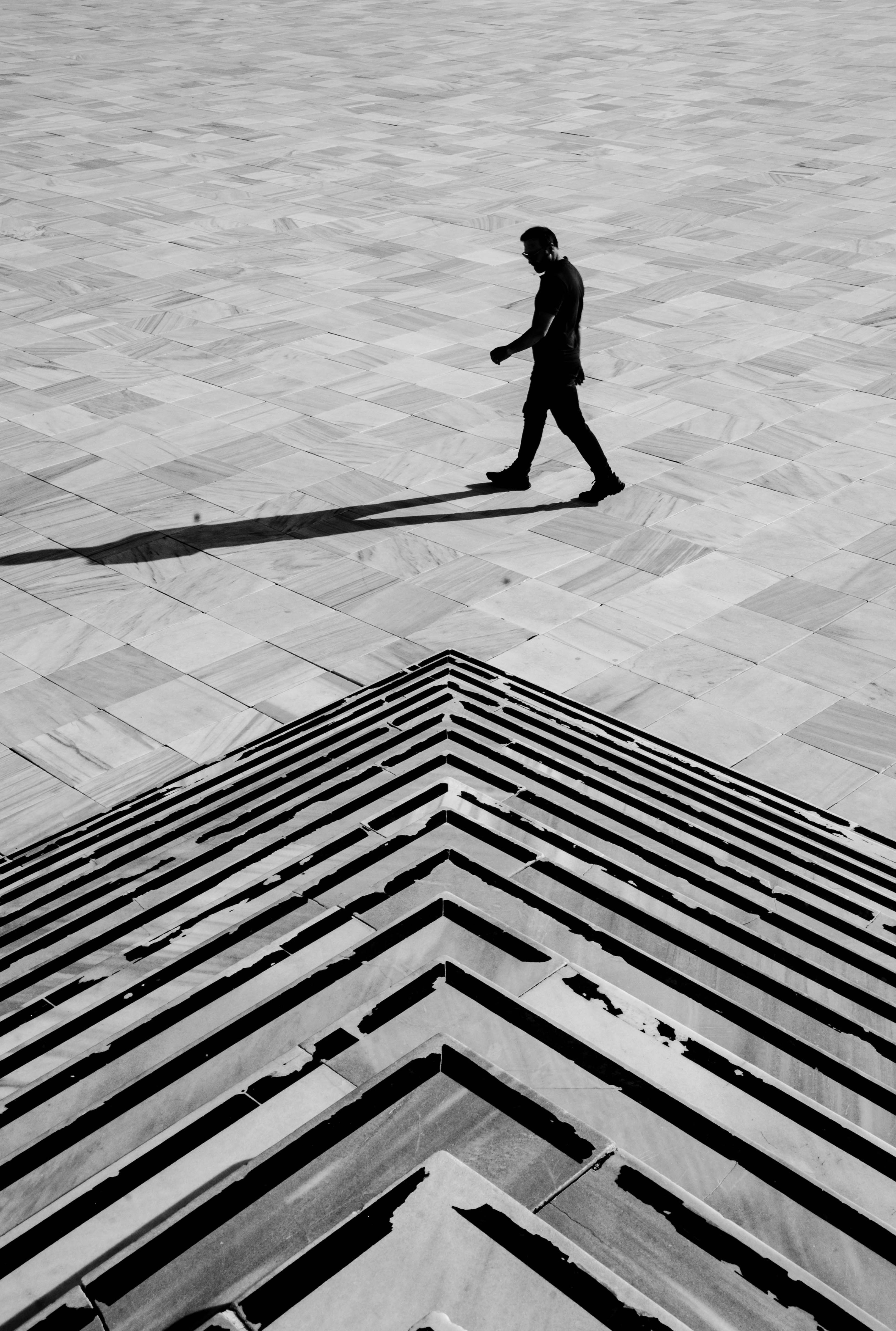 A lone silhouette of a man walking across geometric city steps in black and white.