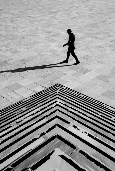 A lone silhouette of a man walking across geometric city steps in black and white.