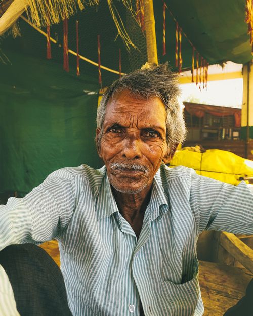 Free Senior man with gray hair and mustache sitting in a green tent, wearing a white striped shirt. Stock Photo