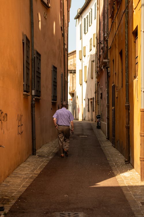 Back View of a Man Walking in a Narrow Alley between Residential Buildings 