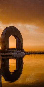 Stunning modern arch-shaped building reflecting on water at sunset.