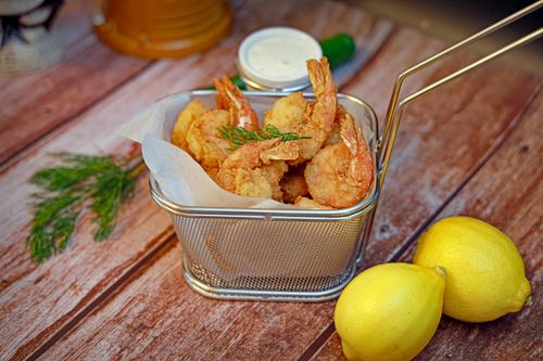 Free Delicious fried shrimp served in a basket with fresh lemons on a rustic wooden table. Stock Photo