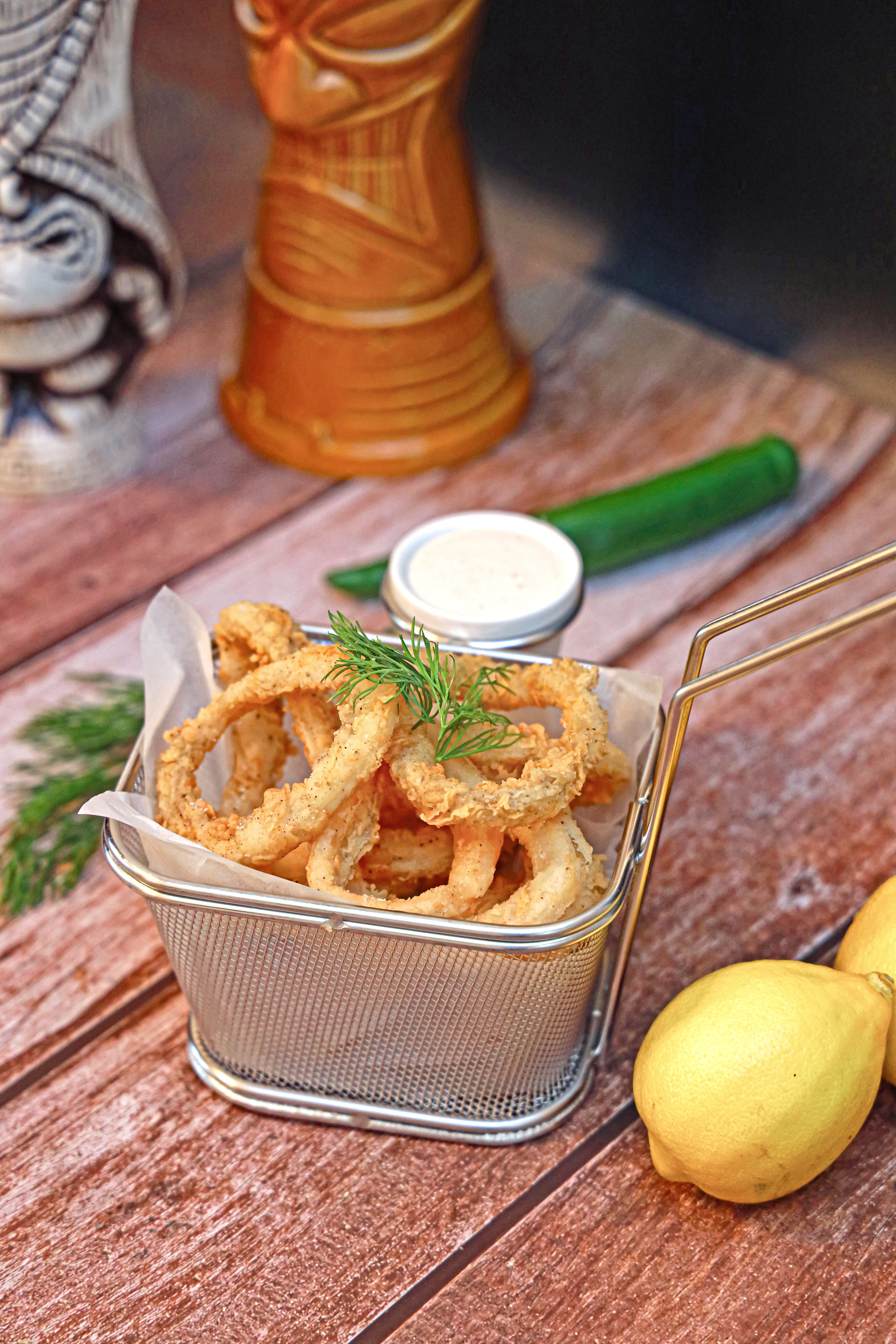 Basket of crispy onion rings served with dipping sauce, garnished with lemon and dill.