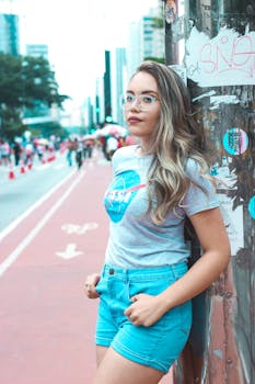 Fashionable woman in blue shorts and glasses posing on a vibrant street, showcasing urban style.