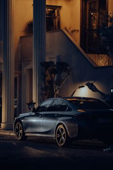 A luxury car parked under soft lighting near grand columns at night in the city, showcasing elegance.
